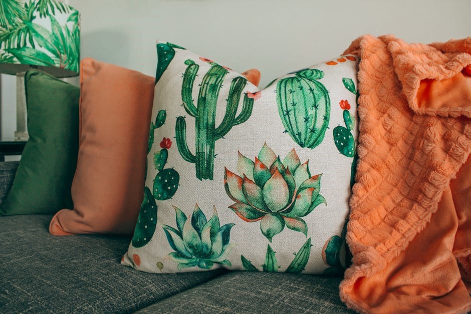 cactus pillow on couch with orange blanket and orange and green pillows on a neutral color grey couch