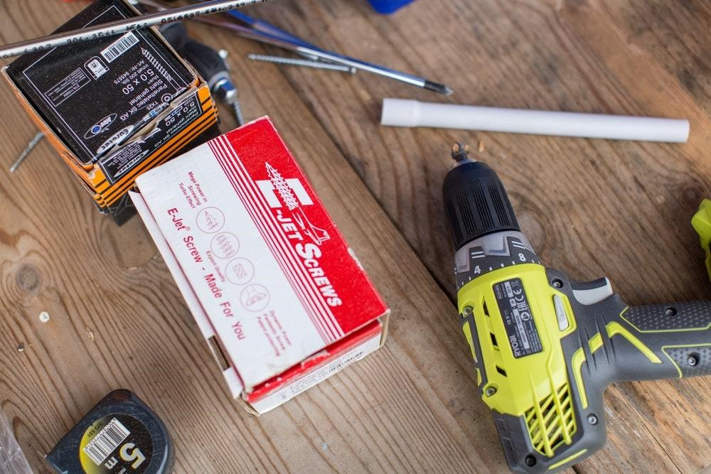 drill on a workbench and a red box of screws on a workbench